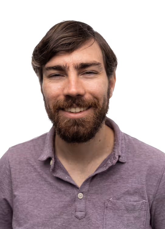 Smiling man with brown hair and beard wearing a purple buttoned shirt.