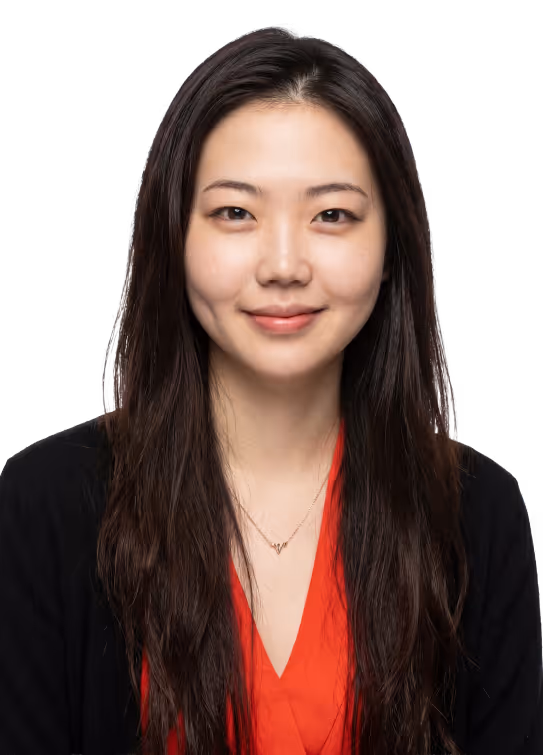 Smiling woman with long dark hair wearing a red top and black cardigan on a white background.