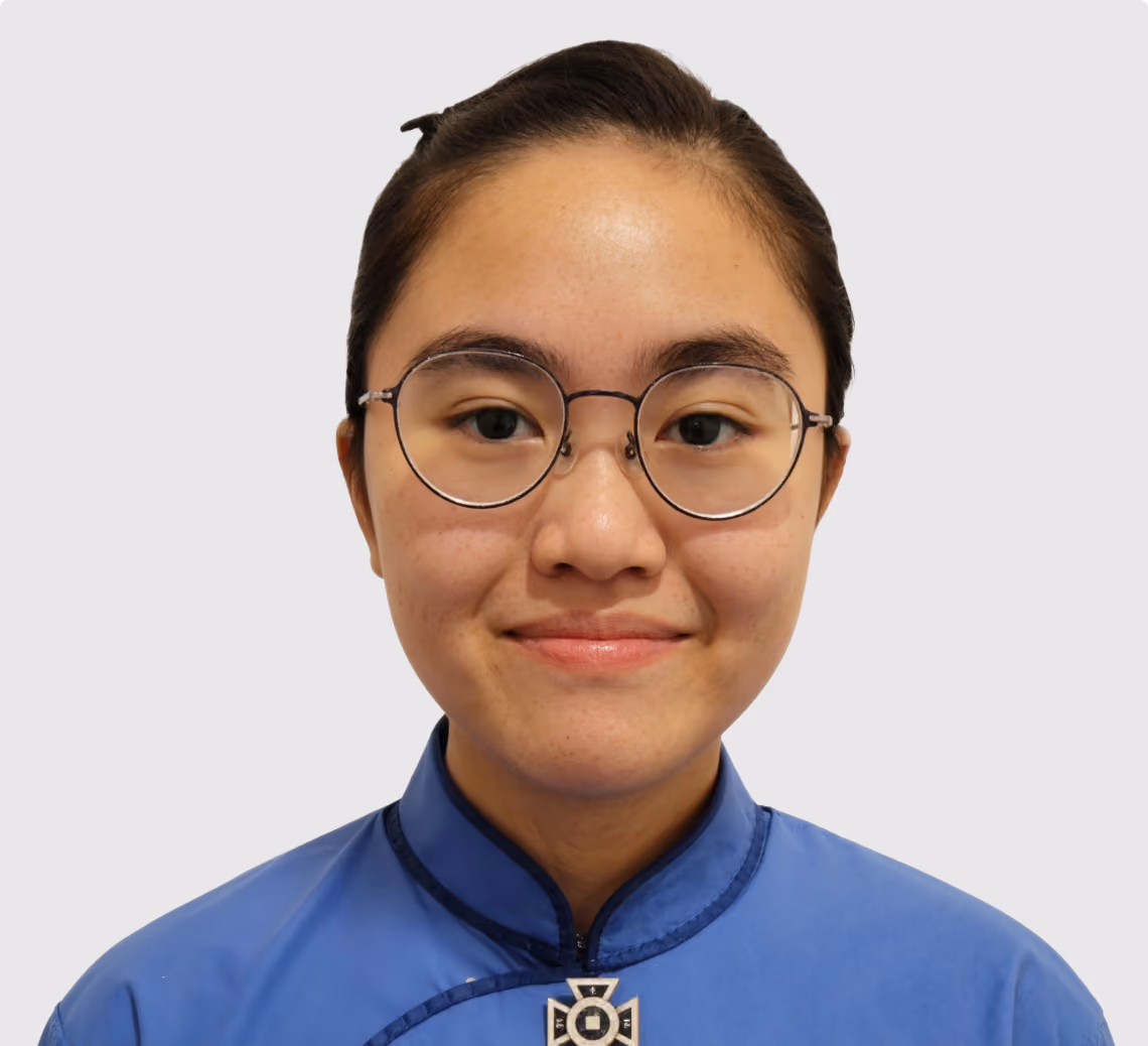 Smiling young woman with round glasses and hair tied back wearing a blue traditional-style top.