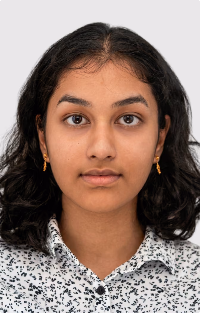 Close-up portrait of a young person with long black hair and round glasses wearing a pink shirt against a gray background.