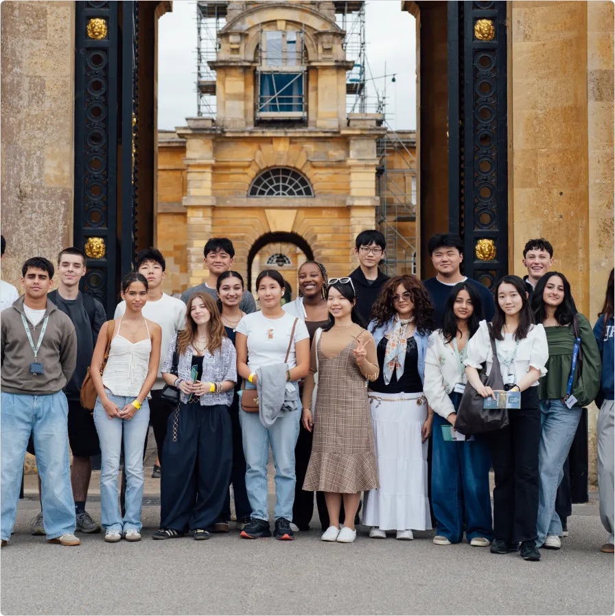 Group of diverse young adults standing in front of a historical stone archway with ornate black and gold pillars.