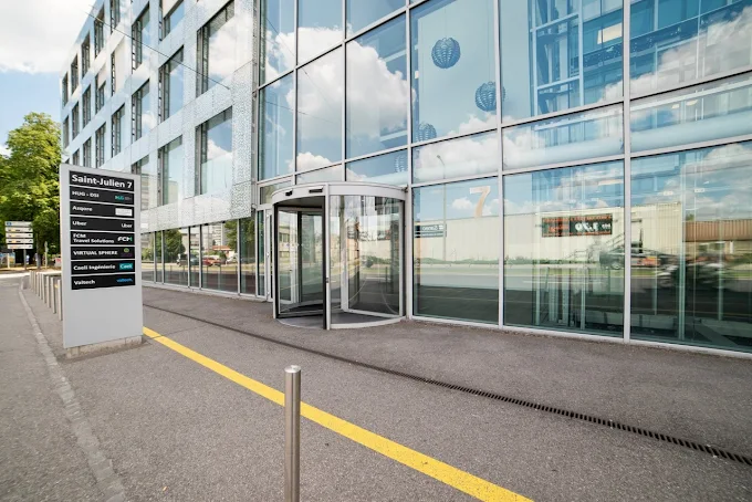 Modern glass building entrance with a revolving door and a directory sign listing company names.