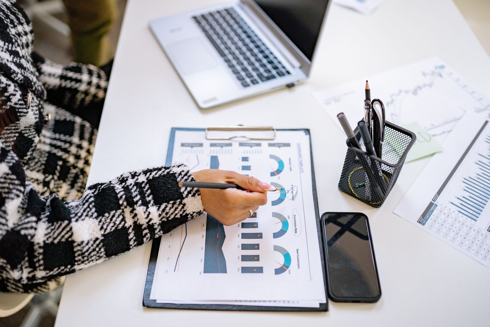 Une personne analyse des graphiques sur des documents, à côté d’un ordinateur portable et d’un téléphone.