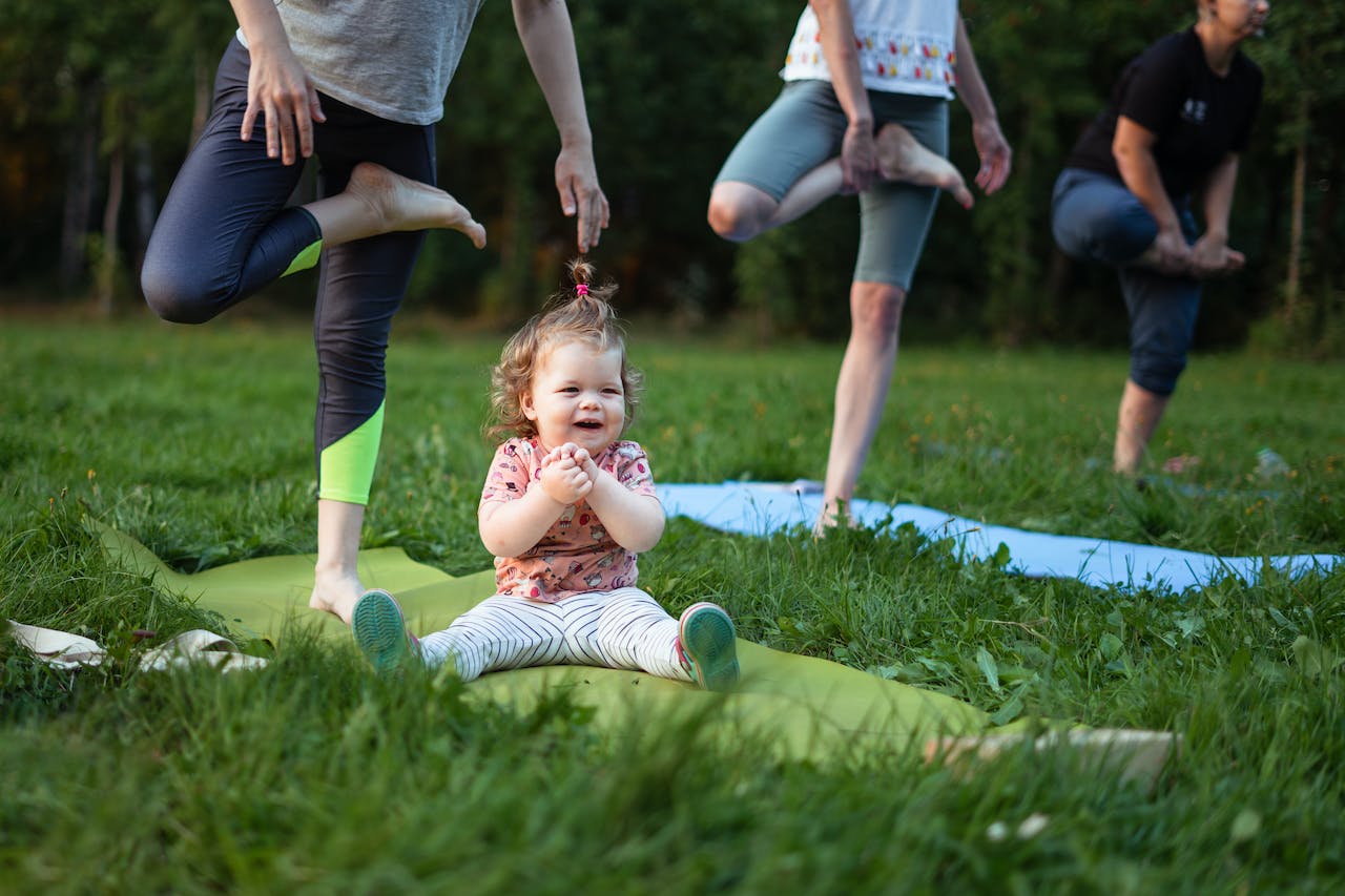 a group of people doing yoga outside with a child sitting on a yoga mat