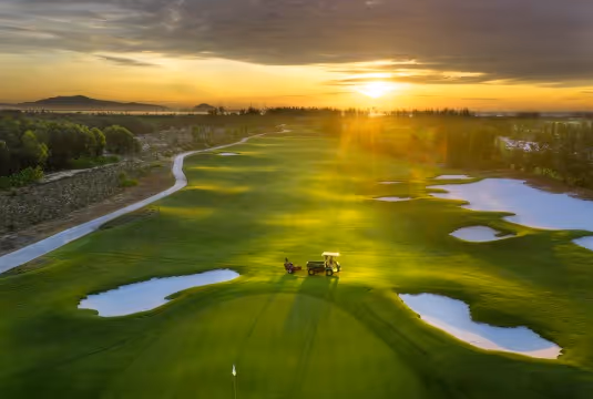 A tranquil golf course at dusk, with a few golfers enjoying the peaceful atmosphere.