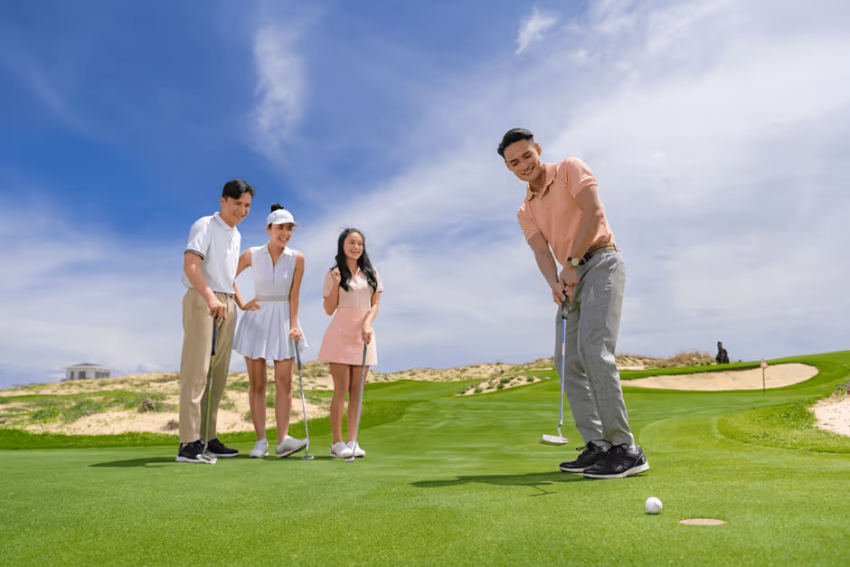 A family playing golf together on a green course in Vietnam, with parents guiding their children.