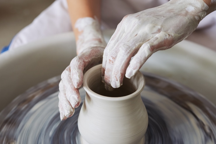 Hands of unrecognizable female potter making clay vase on throwing wheel 