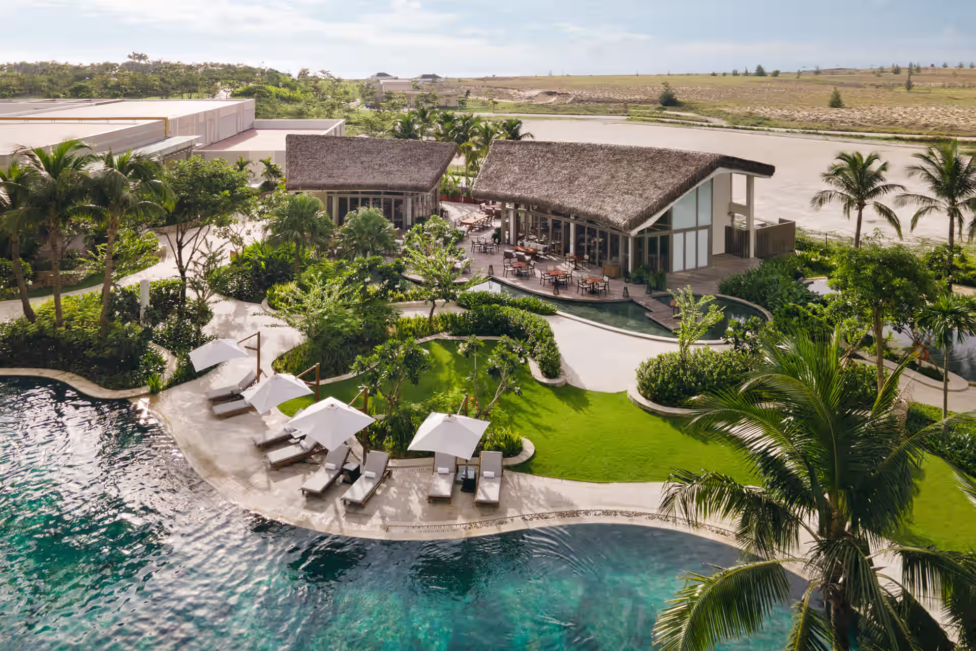An aerial view of Charred reveals its open-air pavilion, winding pool and sunlit loungers framed by lush resort gardens