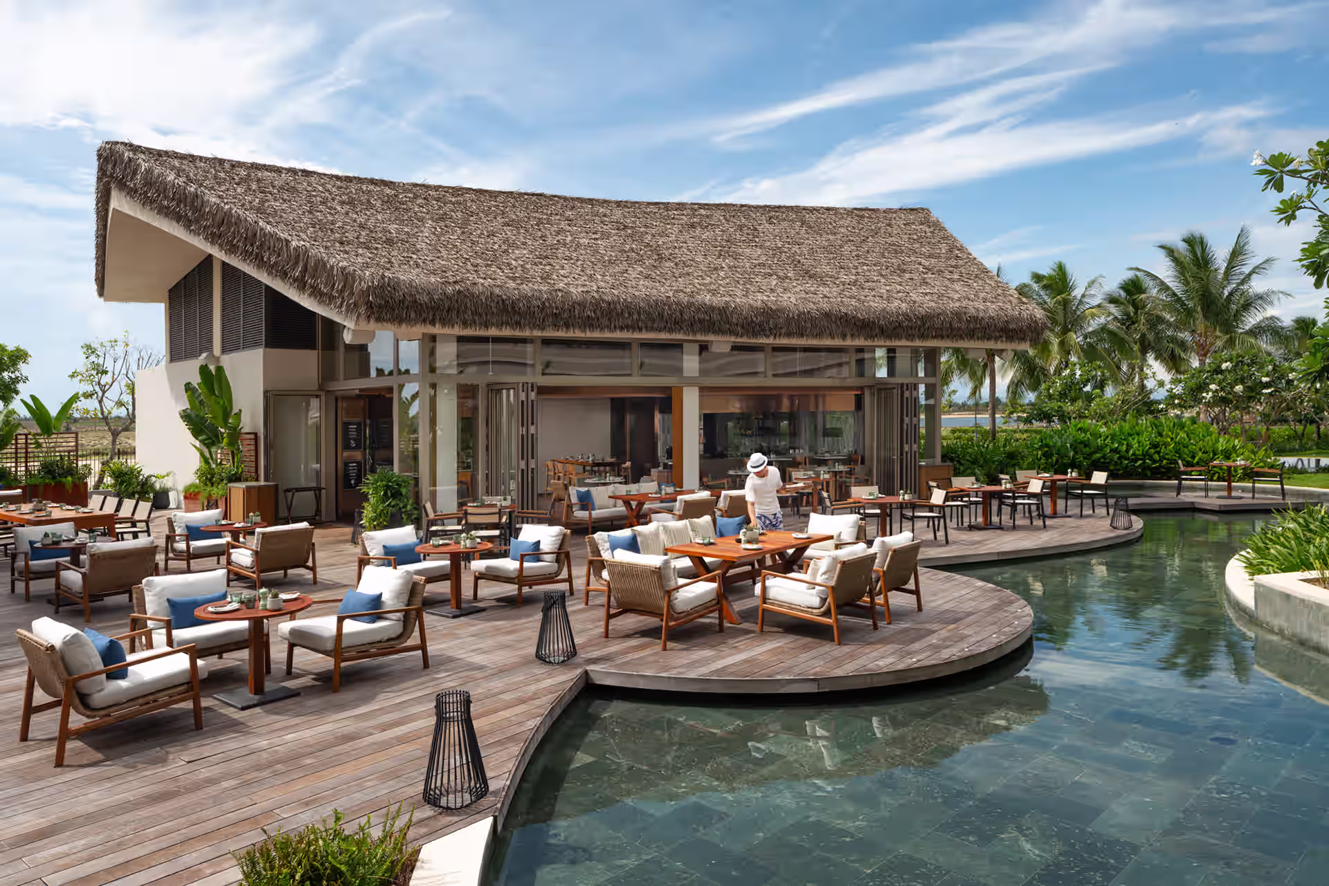 Open-air tables and relaxed lounge seating stretch along the water, creating an inviting setting for casual poolside dining