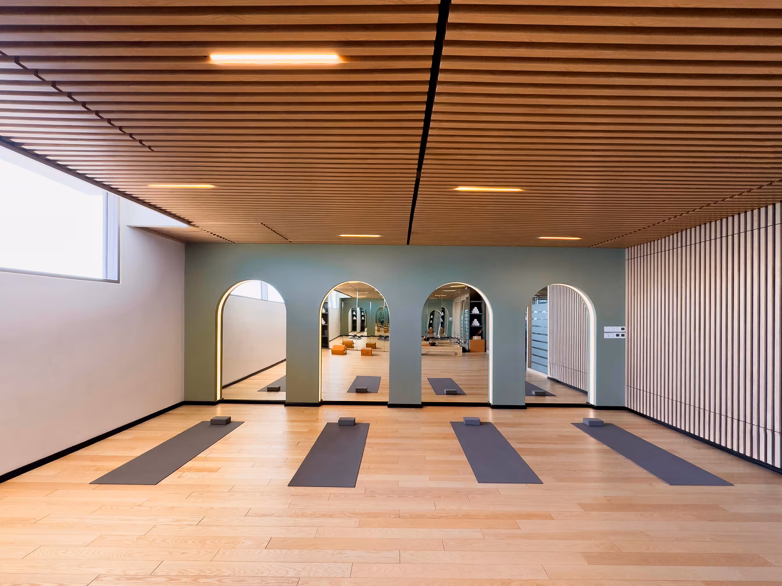 Sunlit yoga studio with wooden floors, exercise mats and softly illuminated arched wall features.
