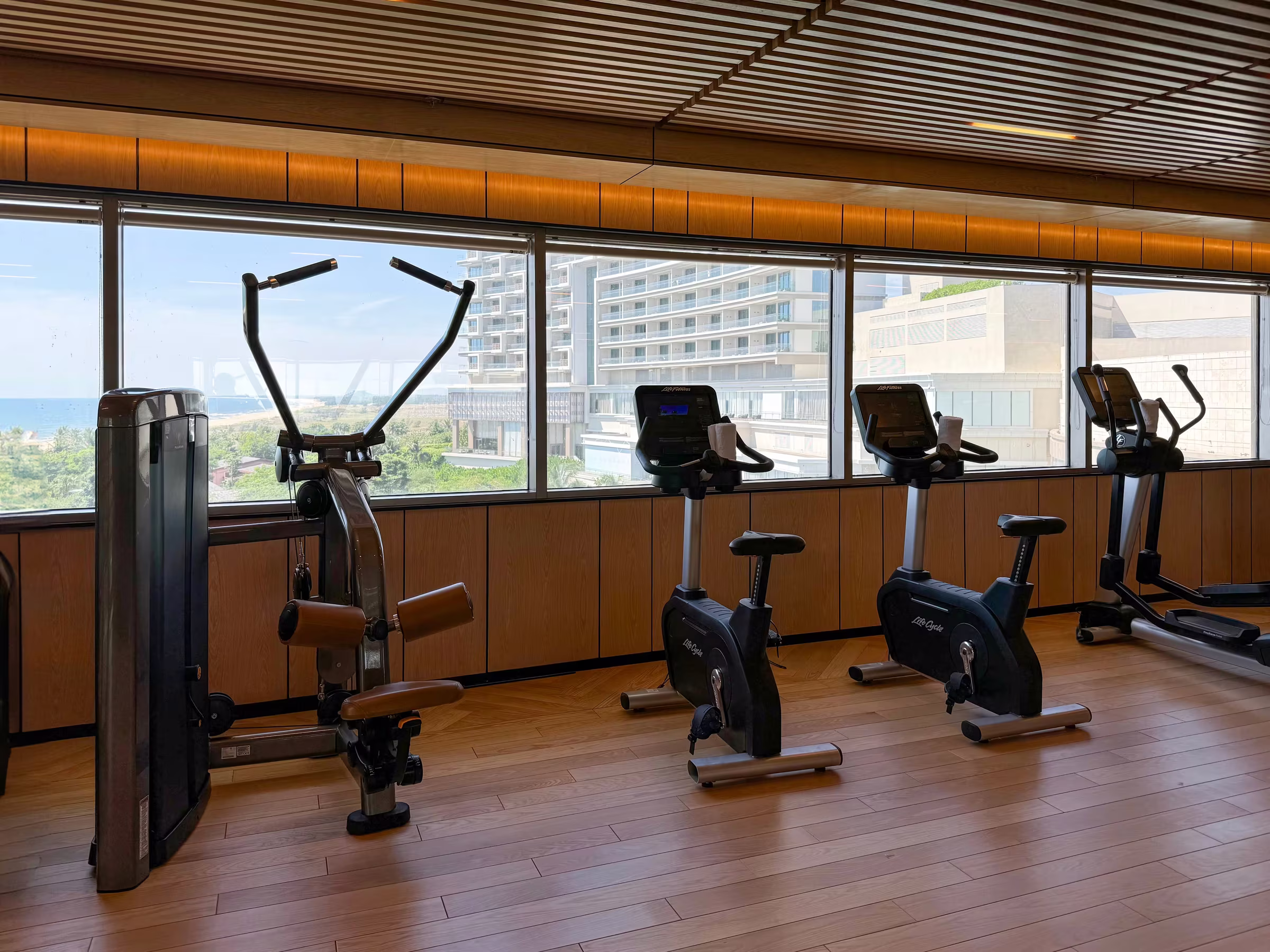 Stationary exercise bikes lined up beside floor-to-ceiling windows overlooking the resort.