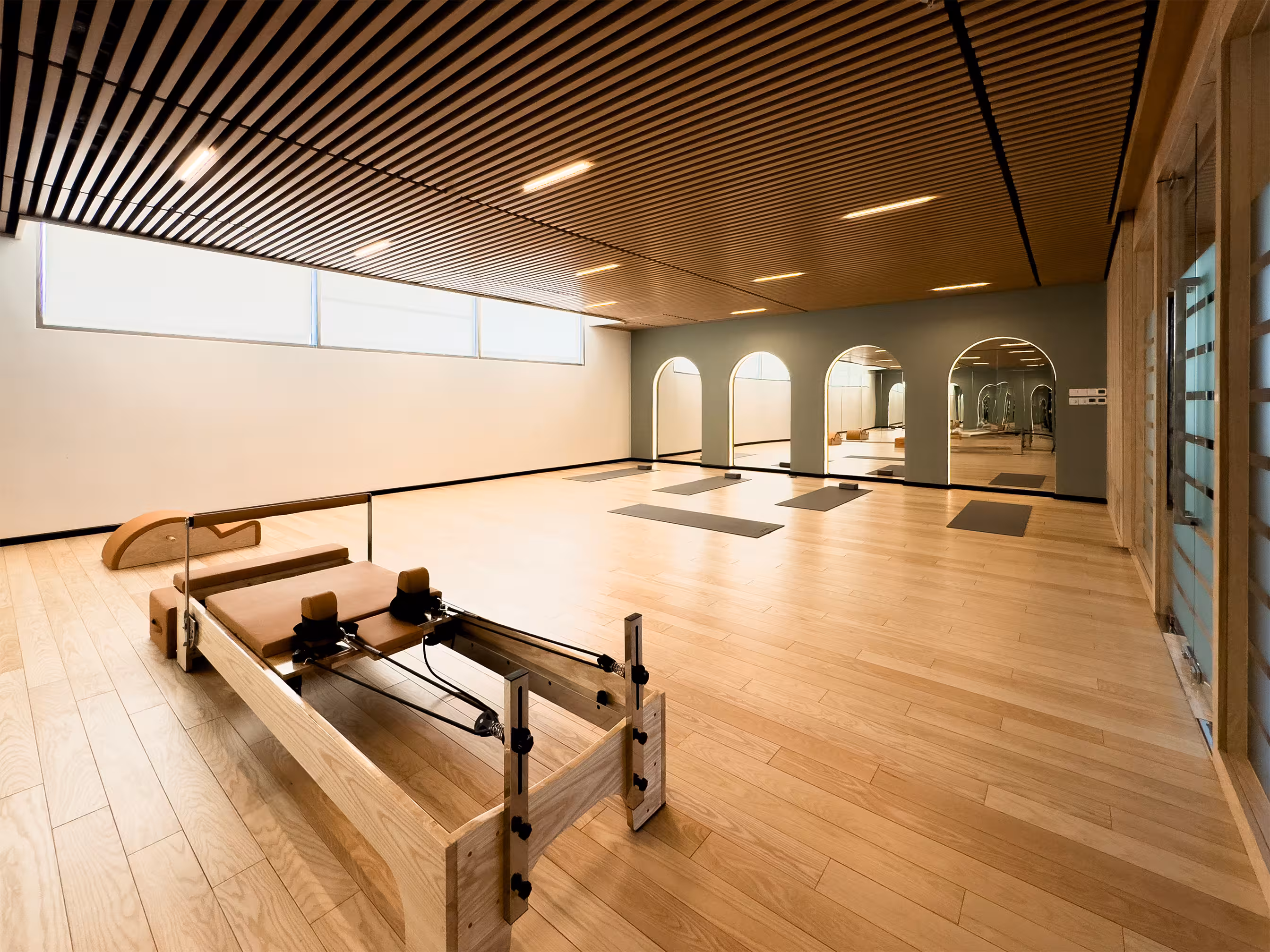 Open Pilates studio with wooden barrel equipment, mirrored walls and calming natural finishes.