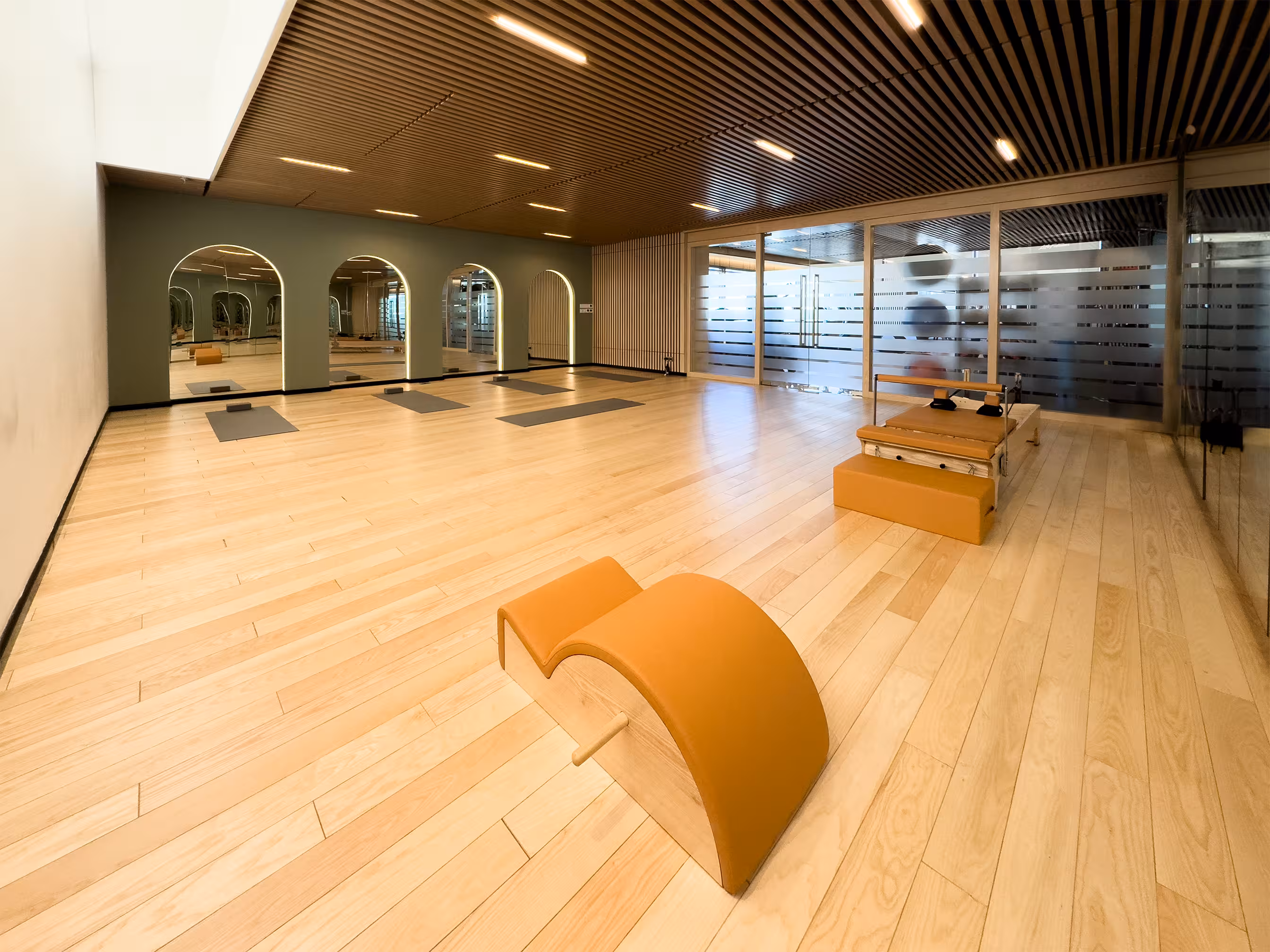 Pilates reformers arranged in a bright studio with mirrored walls and warm wood details.