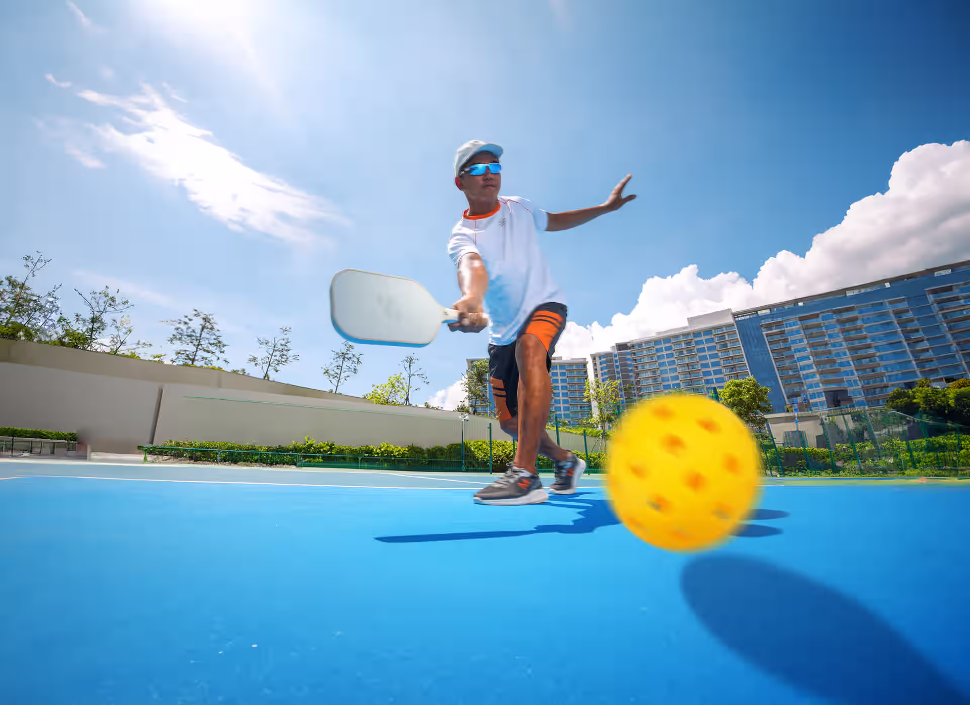Low-angle action shot of a pickleball player returning the ball on a bright blue outdoor court.