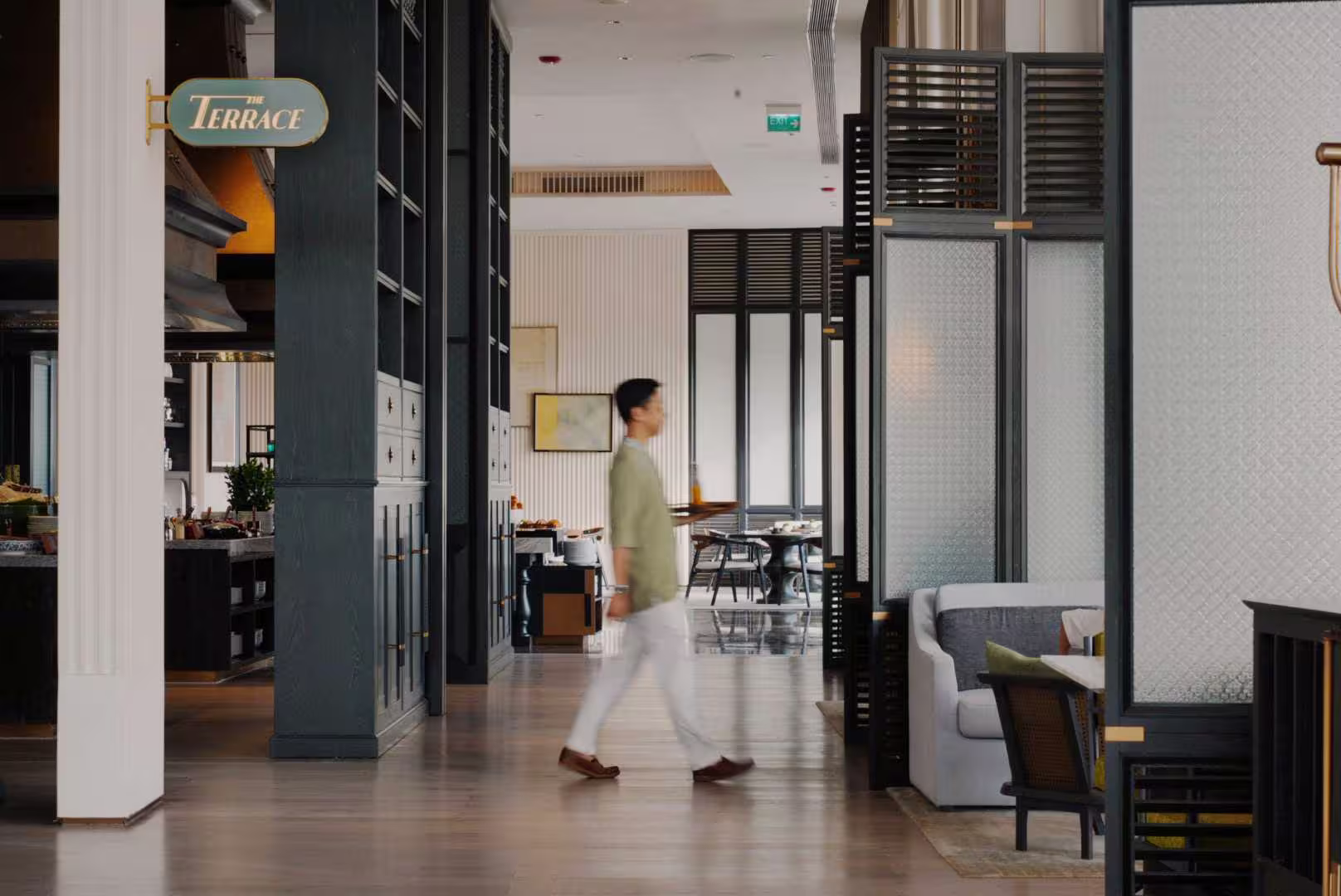 The Terrace restaurant at Hoiana Hotel & Suites, with a server carrying refreshments through bright interiors framed by dark timber accents