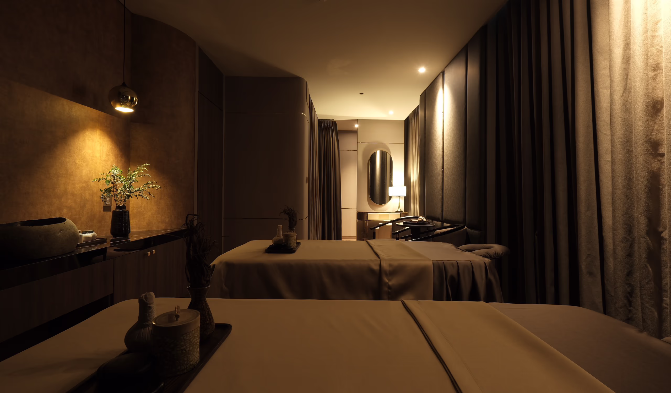 Couples’ treatment room at Tinh Spa with two massage beds, soft lighting and floor-to-ceiling curtains.