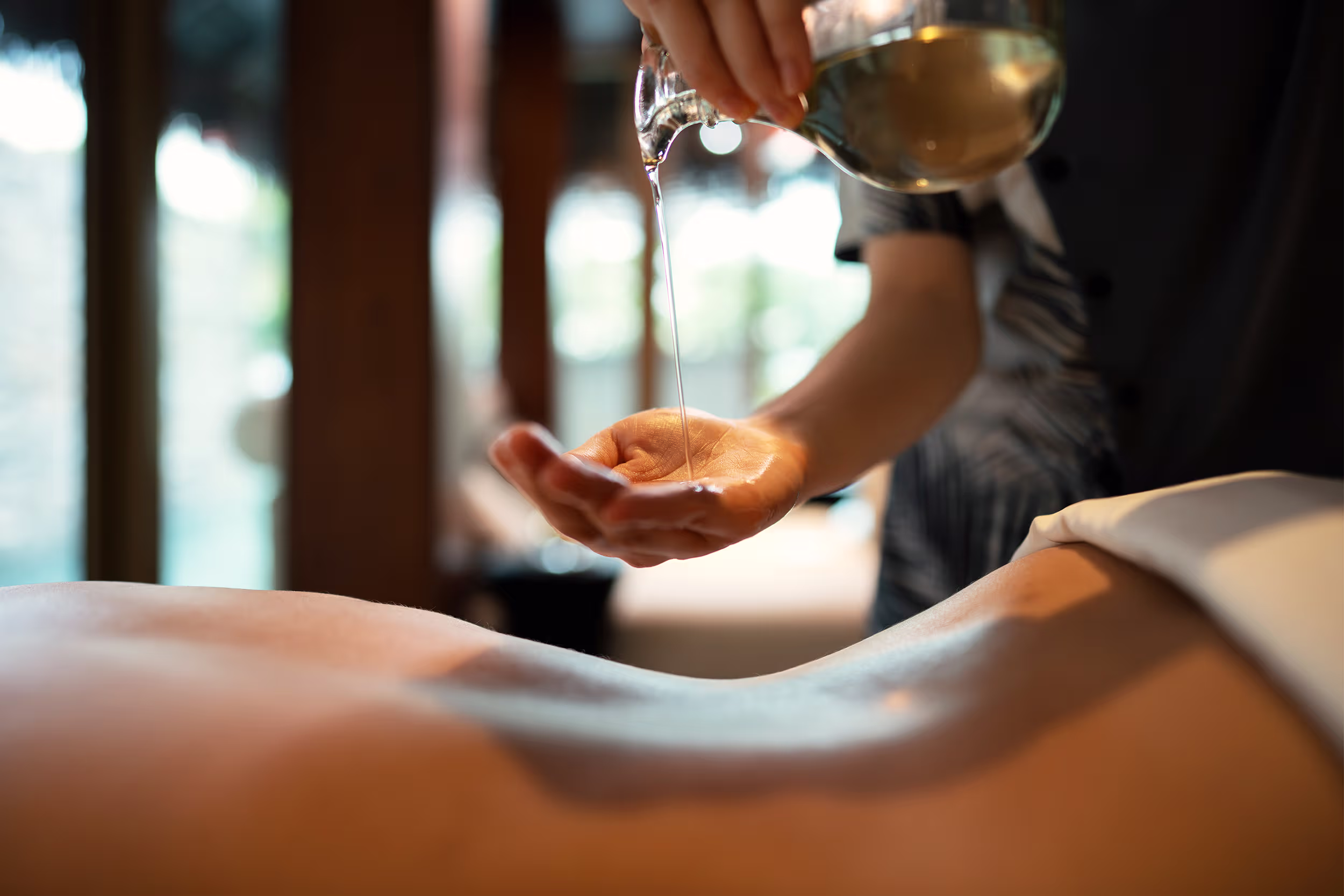 Close-up of a warm oil massage at Downtime Renew as a therapist prepares the treatment over the guest’s back.
