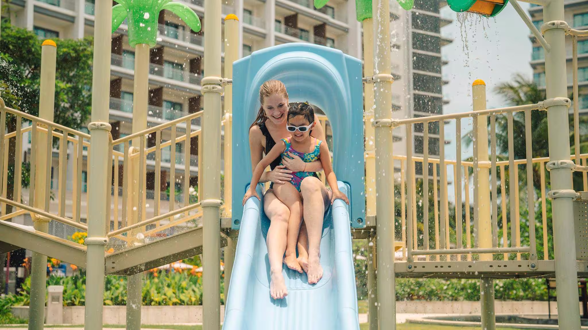 A child riding the waterslide at New World Hoiana Hotel family pool beside a wooden play structure.