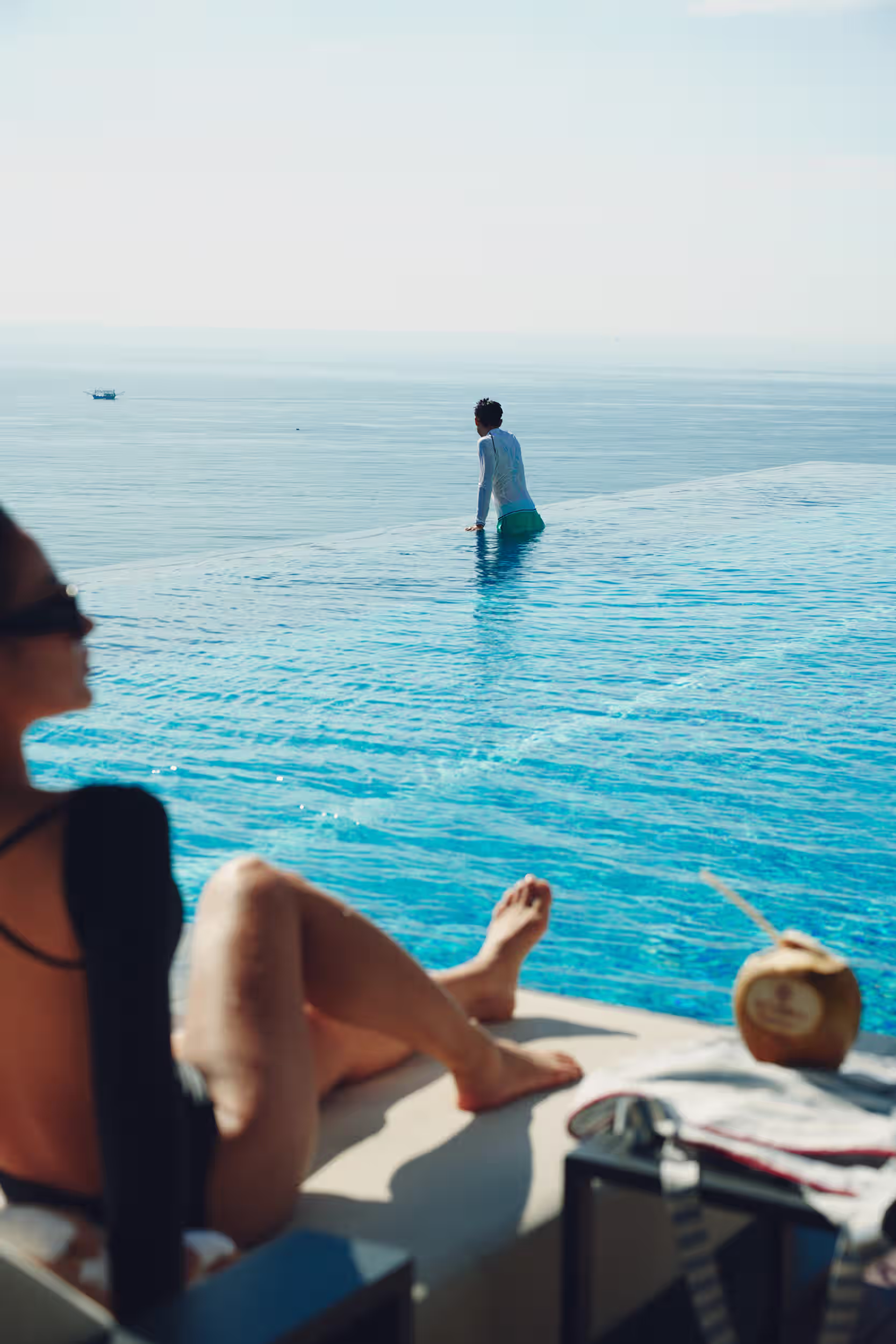 A guest relaxing poolside as another swims in the ocean-facing infinity pool at Hoiana Hotel & Suites.