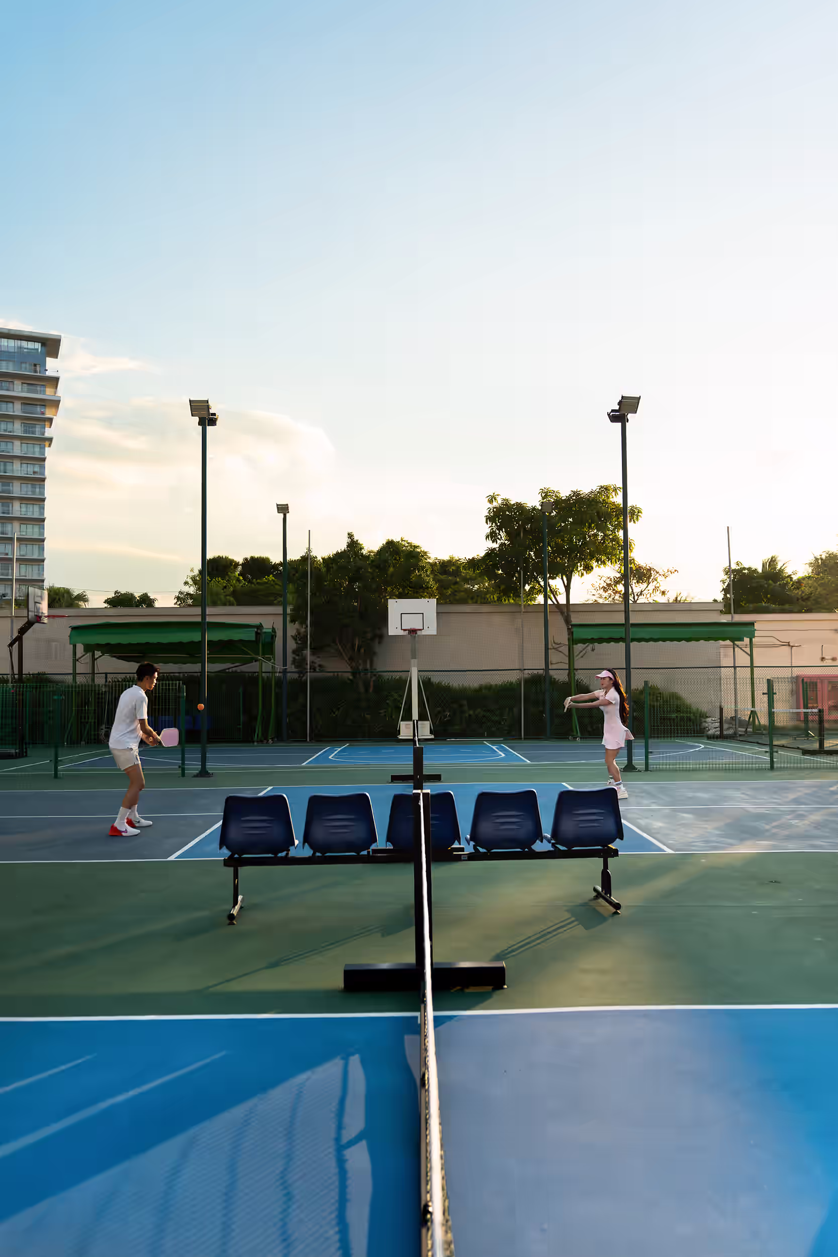 Two guests enjoying a pickleball match on the outdoor court at Hoiana Resort & Golf in the warm late-afternoon light.
