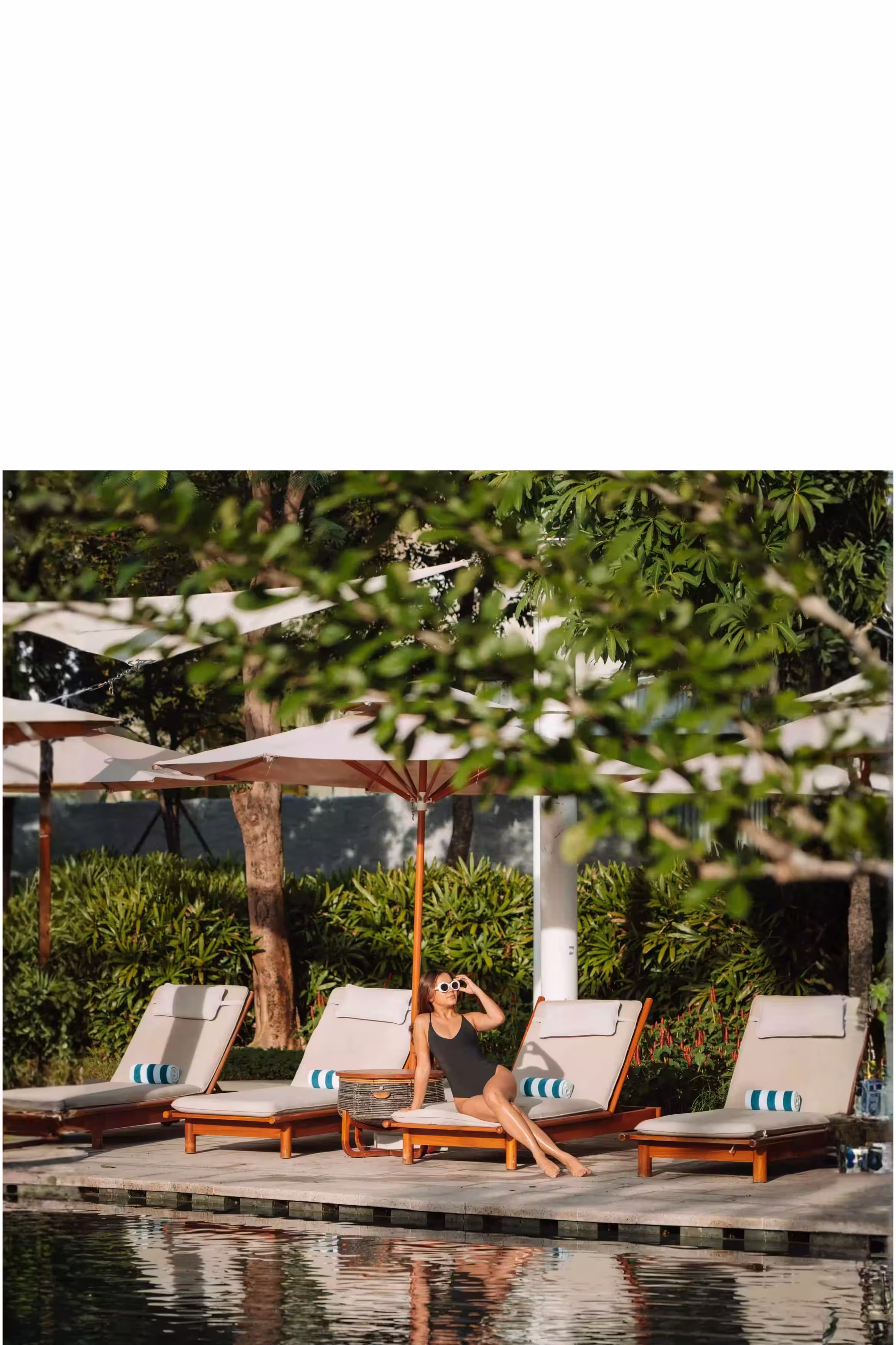 A family relaxing beside the New World Hoiana Hotel family pool, surrounded by tropical greenery and shaded loungers.