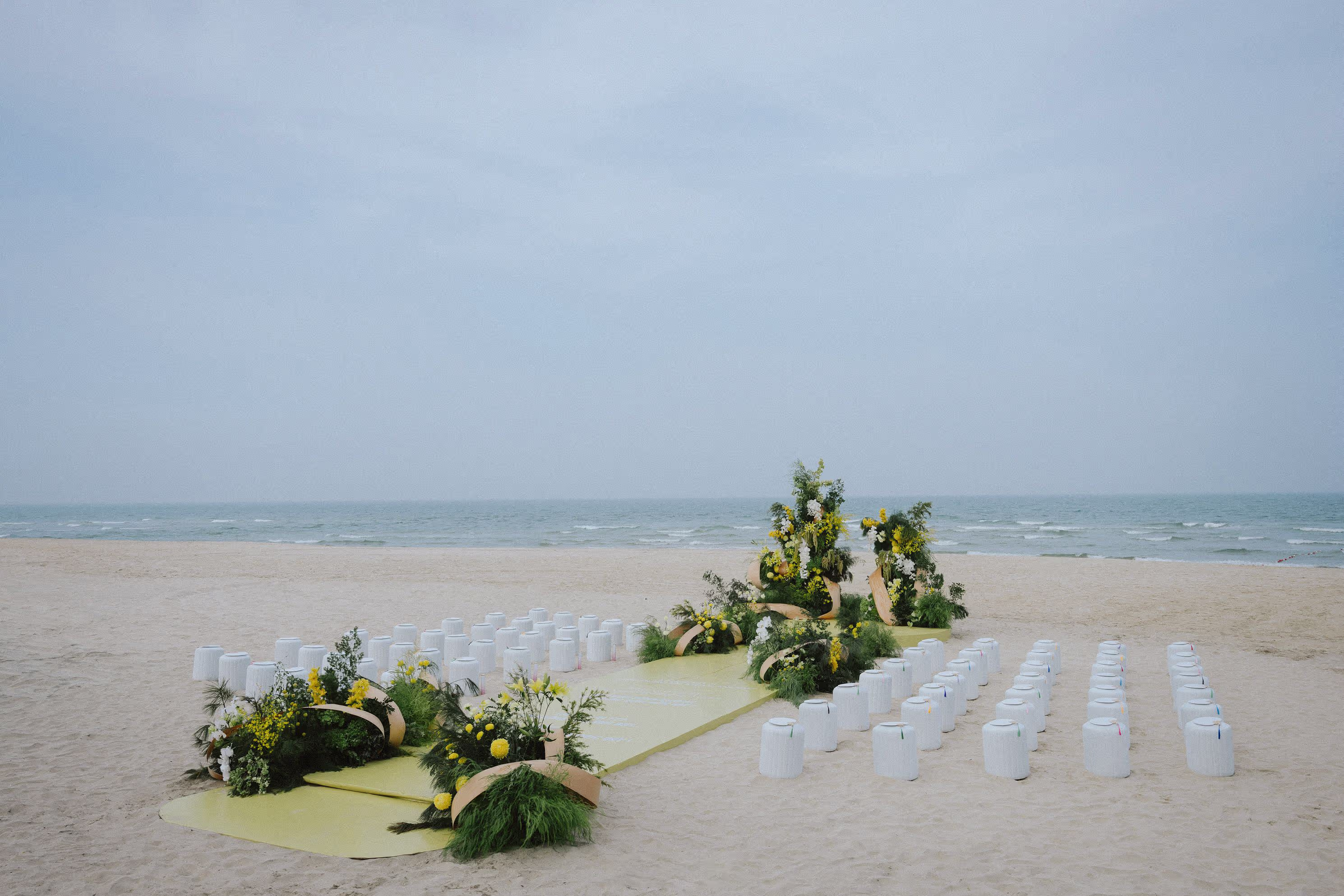 Beachfront wedding venue at The Beach, Hoiana, where a soft green aisle, white seating and sculptural florals frame an intimate ceremony by the sea.