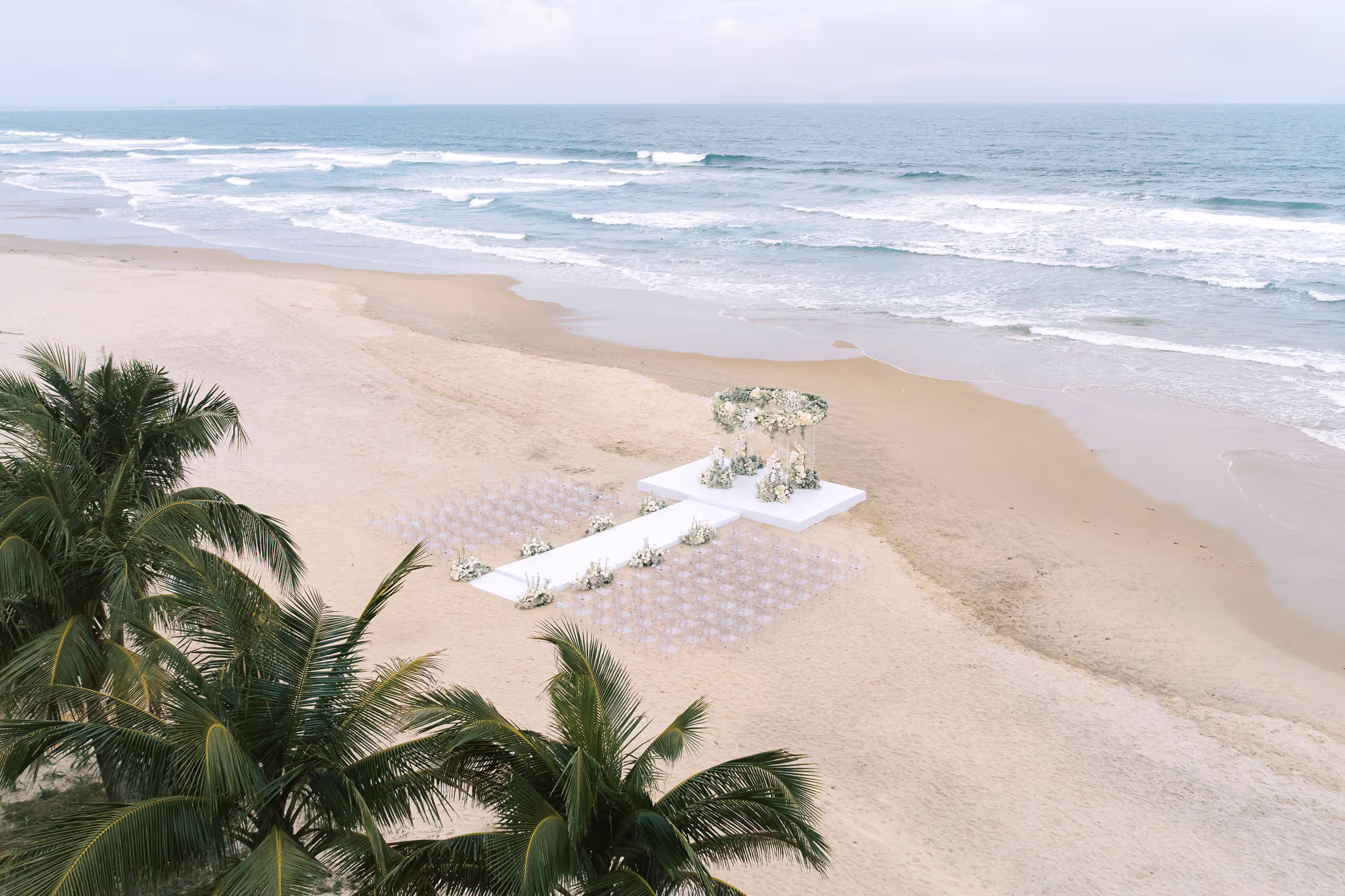 An aerial view reveals a private beachfront ceremony with a white aisle stretching toward the shoreline