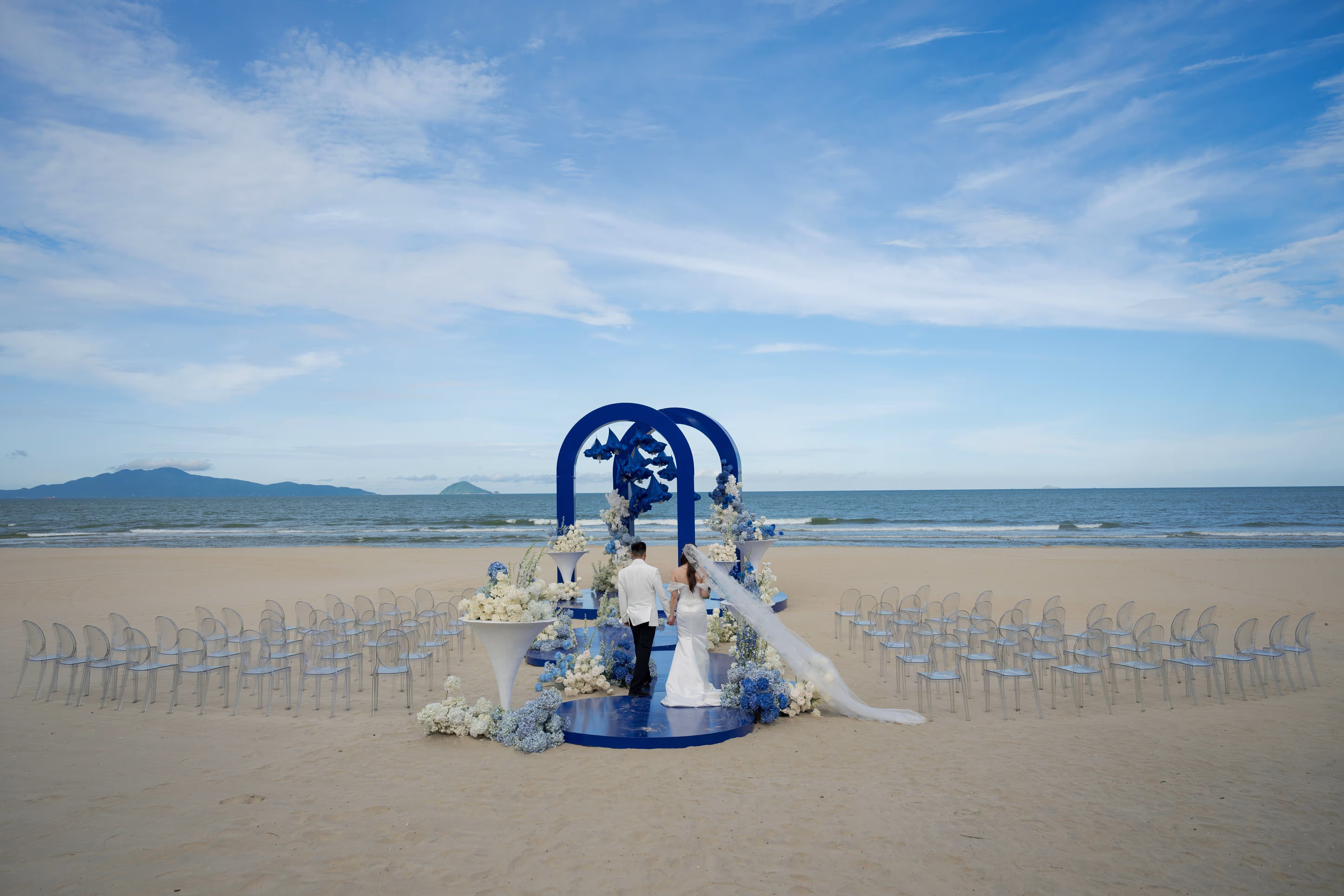 A blue-and-white wedding ceremony brings a fresh coastal palette to the sand beneath an expansive sky