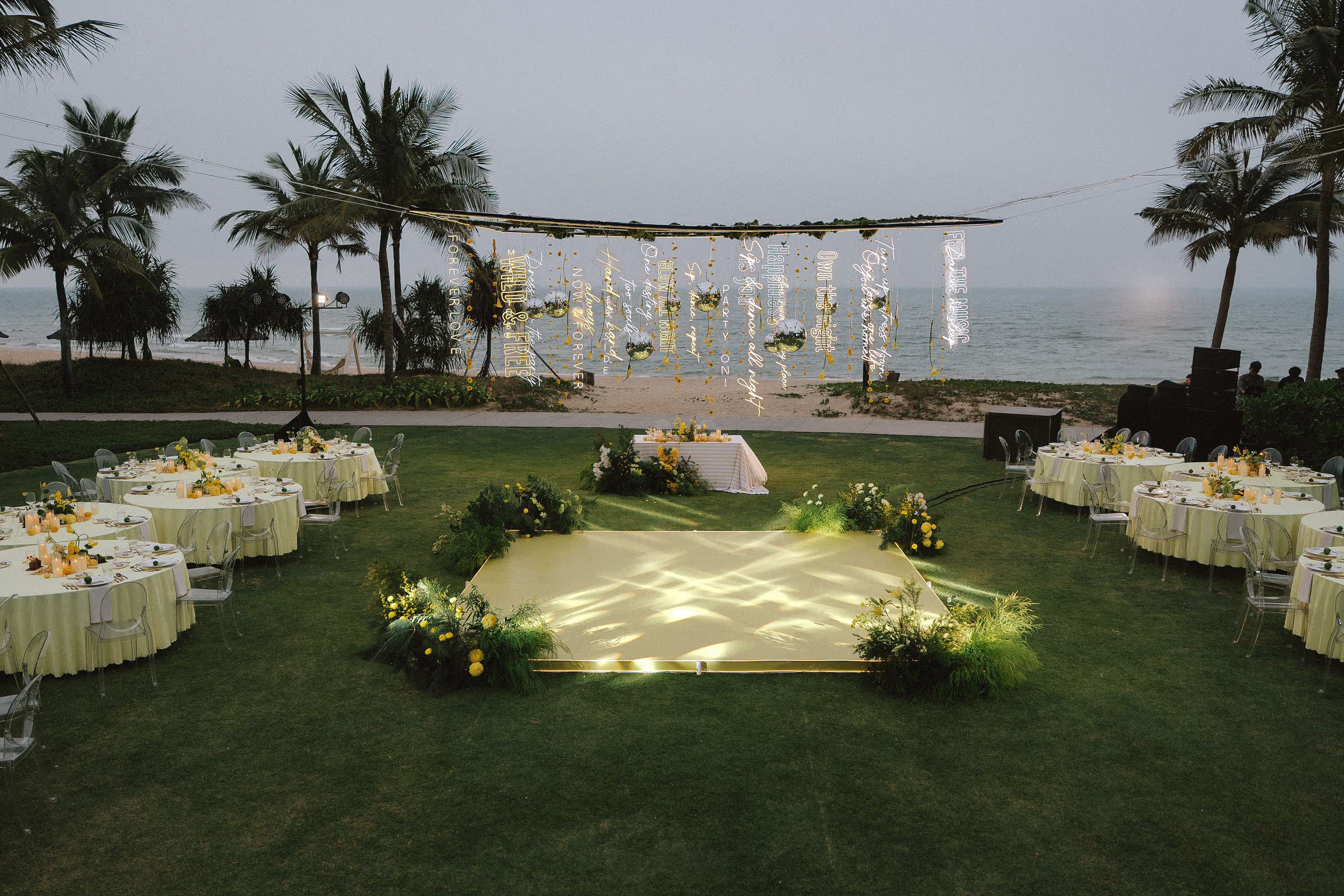 An illuminated wedding aisle and white banquet tables transform the beachfront lawn for an evening celebration