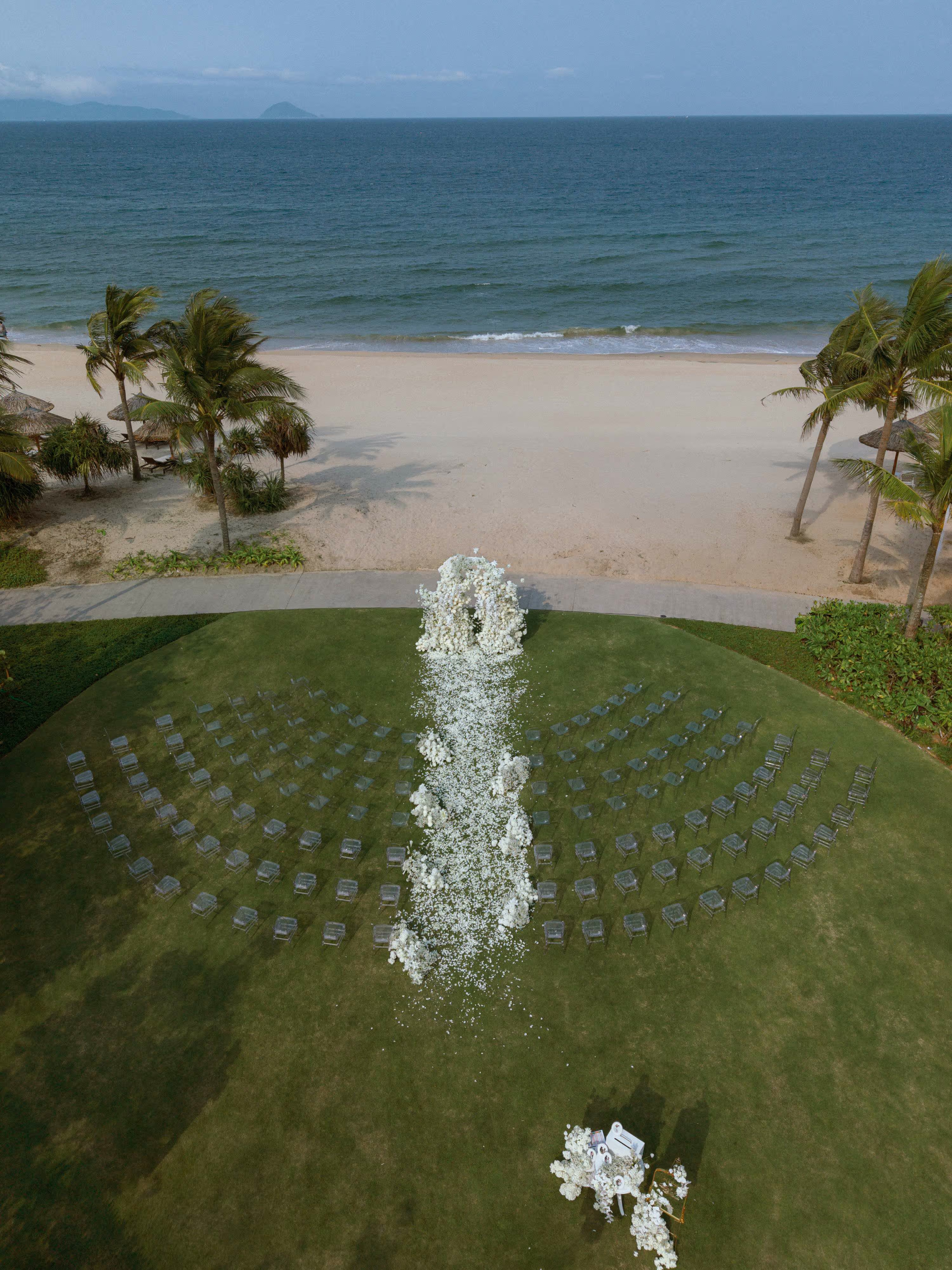 A white floral aisle leads across the manicured lawn toward a ceremony backdrop overlooking the ocean