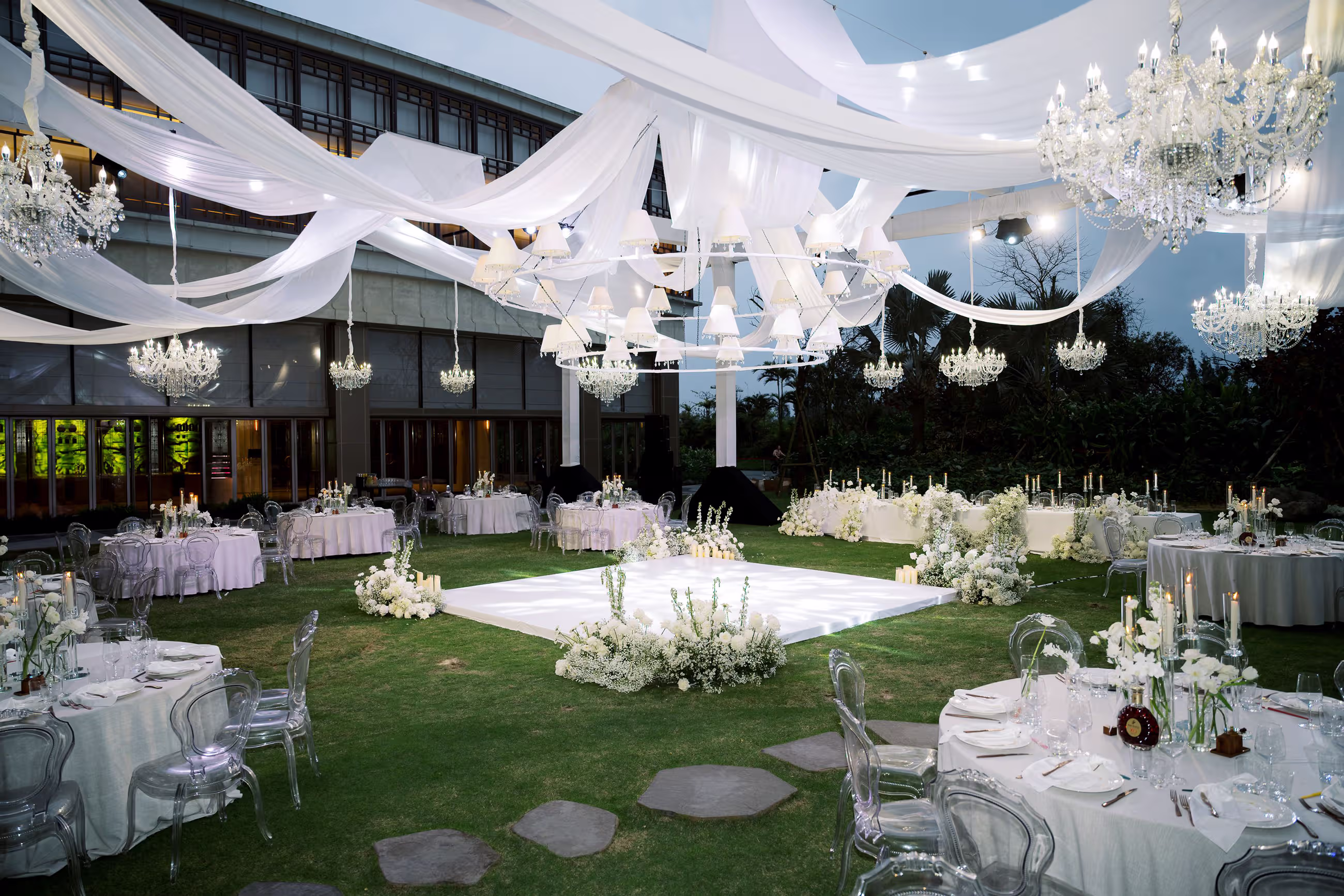 Layered ceiling drapes, hanging lights and white floral tables transform the lawn into a graceful open-air banquet setting