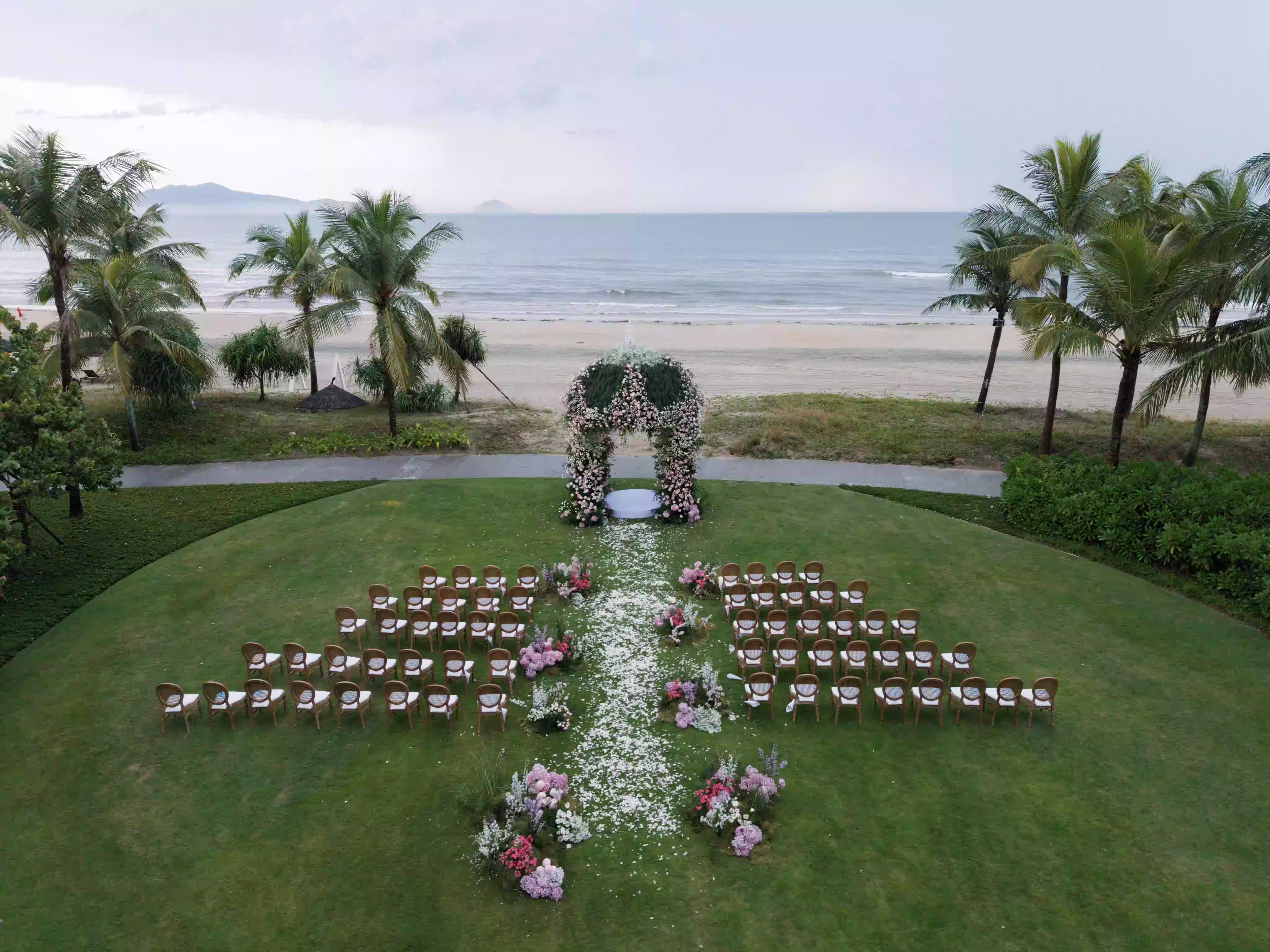 A daytime wedding ceremony unfolds on the lawn with symmetrical seating, floral details and the sea beyond