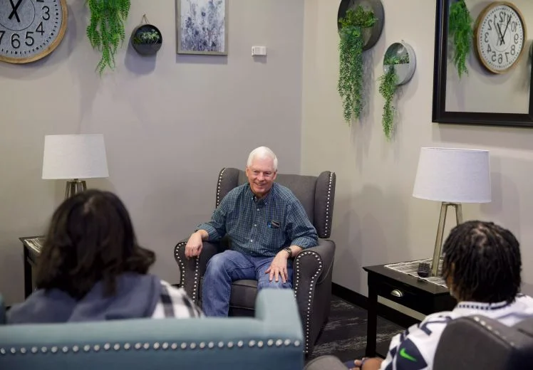Older man sitting in armchair talking with two people in therapy office.
