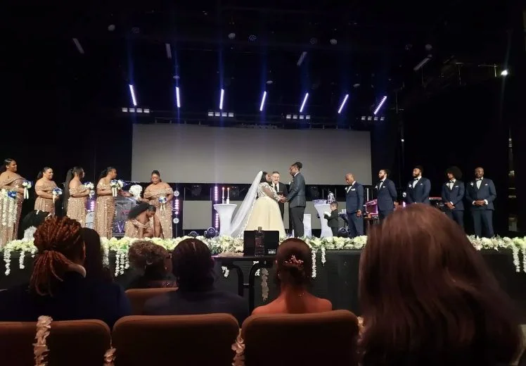 Elegant wedding ceremony with bride and groom on stage, bridal party, dramatic lighting.