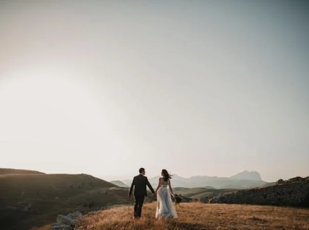 Bride and groom walking hand in hand outdoors at wedding with scenic landscape.