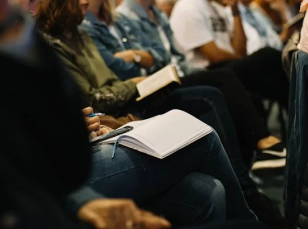 Audience seated with notebooks and pens during a meeting or lecture.