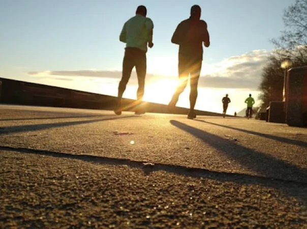 People jogging on a pathway at sunrise casting long shadows.