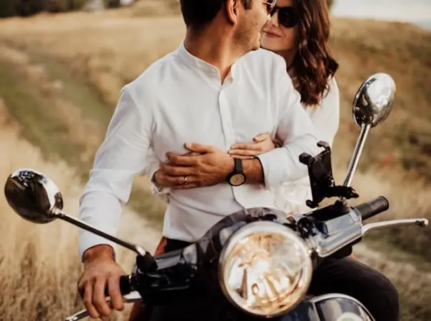 A man and a woman looking at each other on a motorcycle.