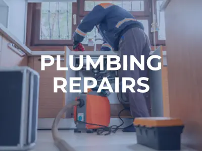 Construction worker performing maintenance on an open sewer line at a roadside construction site near a gas station.