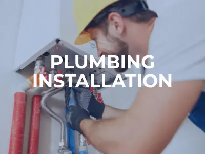 Construction worker performing maintenance on an open sewer line at a roadside construction site near a gas station.