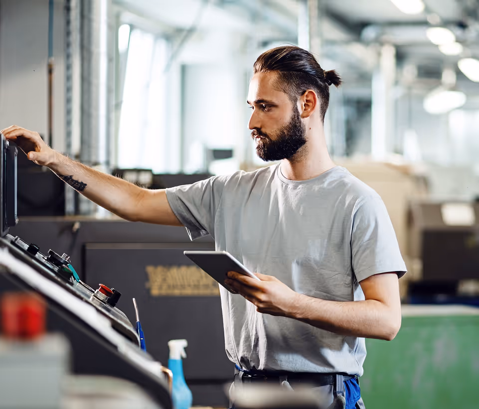 Engineer using a tablet while operating a CNC machine in a factory setting.