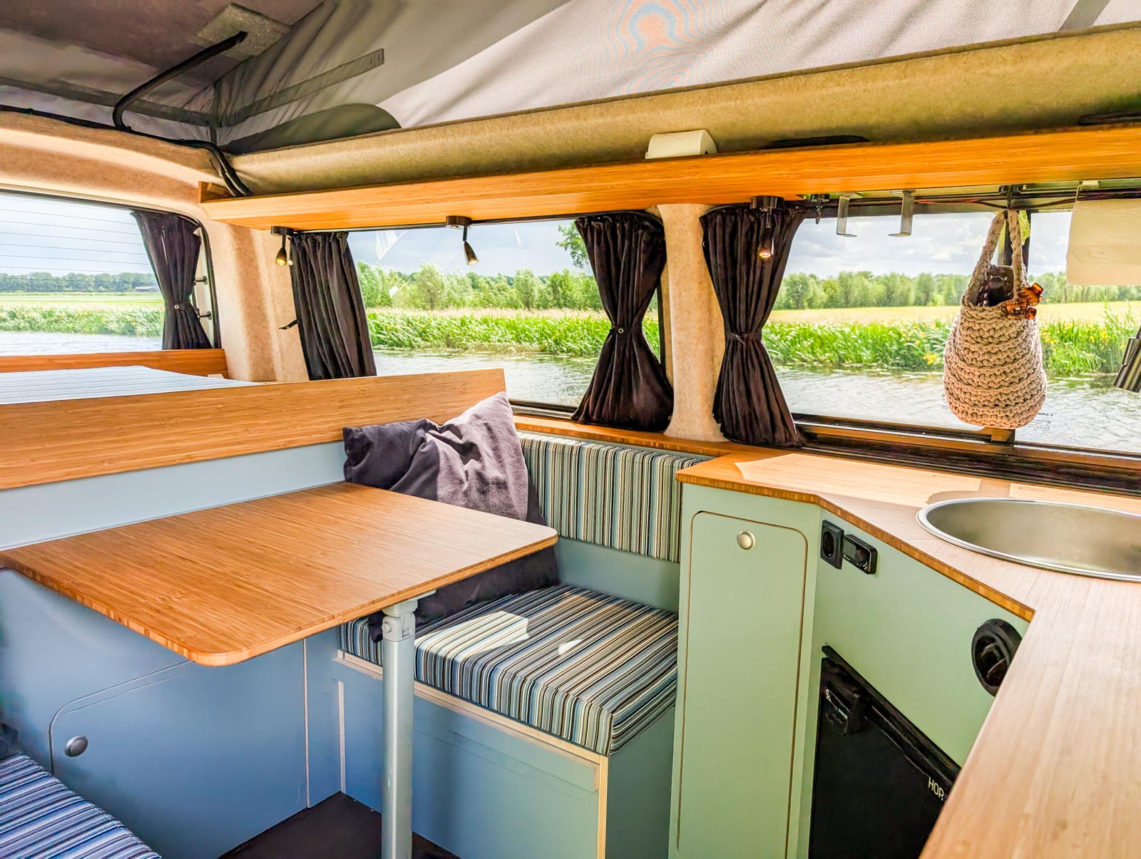 Camper interieur van de kramer met groot bed en keuken die naar buiten kan schuiven en bankje die uitschuifbaar is