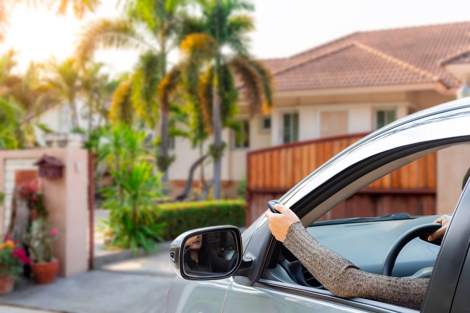 Person arriving to their residence in their car with their hand out the window pressing a button on their garage door opener. 