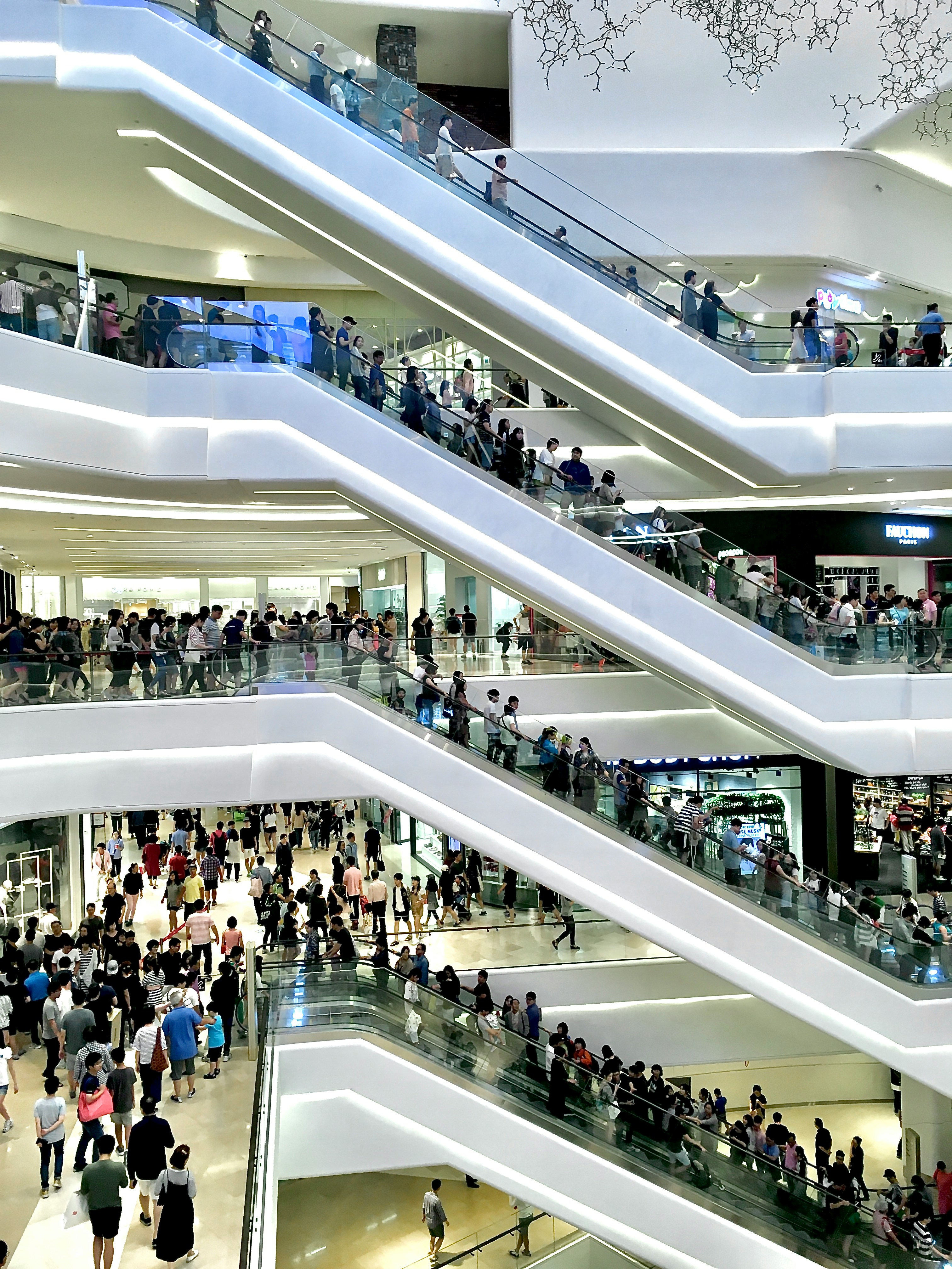 Crowded multi-level shopping mall with many people on escalators and walking in the corridors.