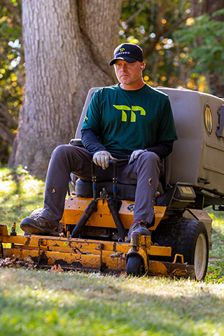 Man wearing a green shirt and cap operating a yellow riding lawn mower in a grassy area.