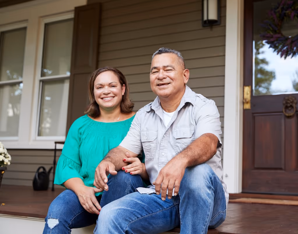 Smiling couple sitting on the porch steps of their home.