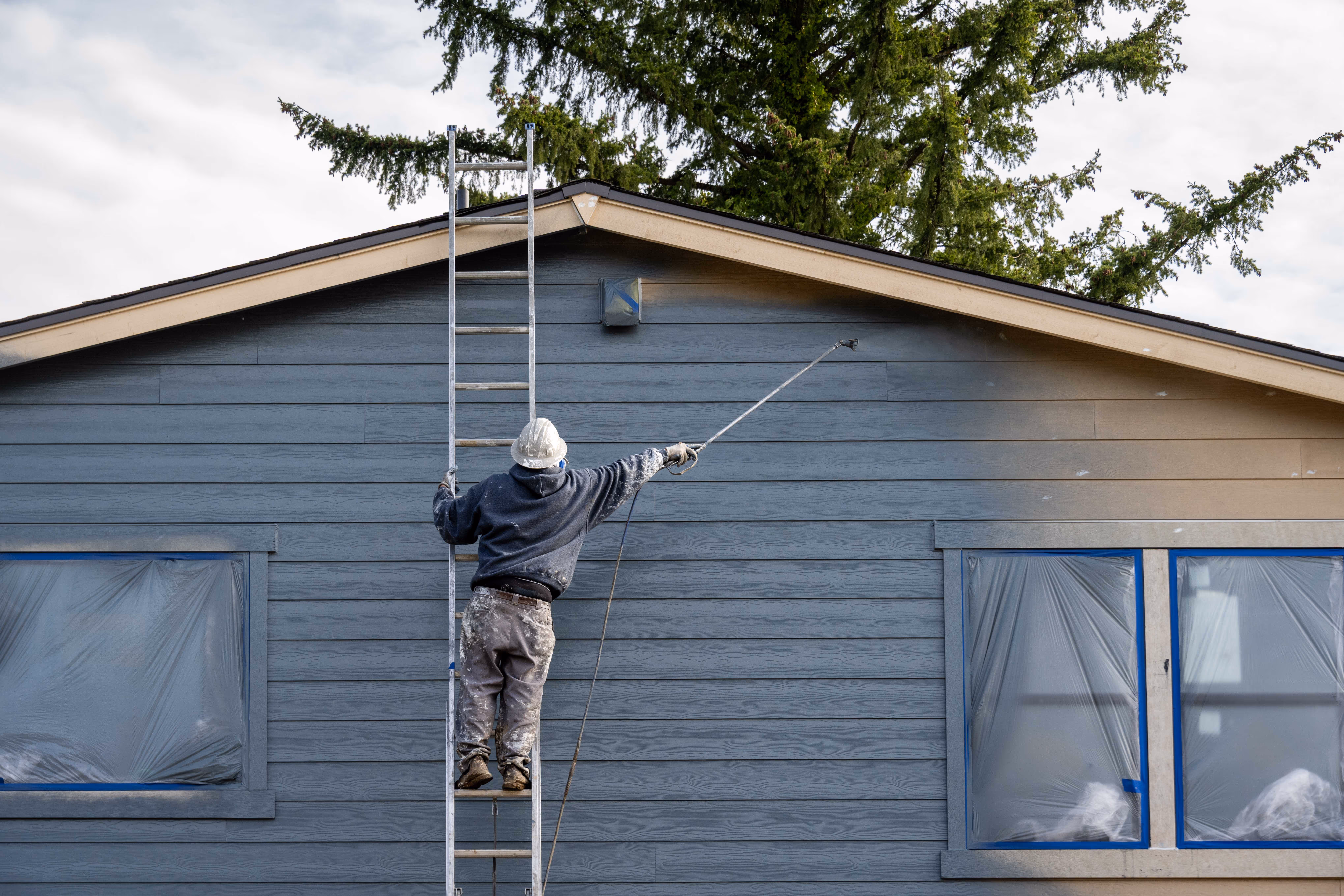 Professional painter using a paint sprayer on an exterior home wall.