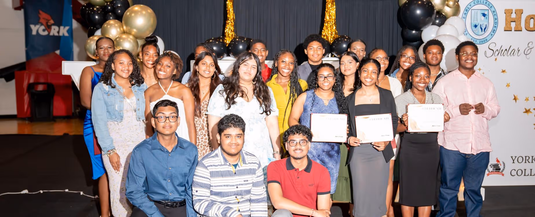 Group of students on stage holding certificates and awards.