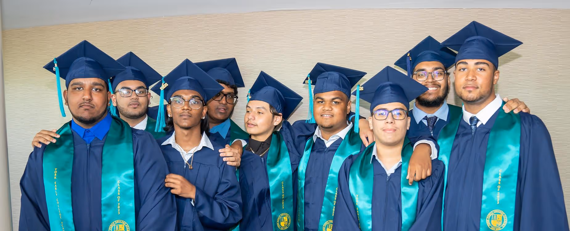 Graduating students in blue gowns and green stoles posing for a group photo.
