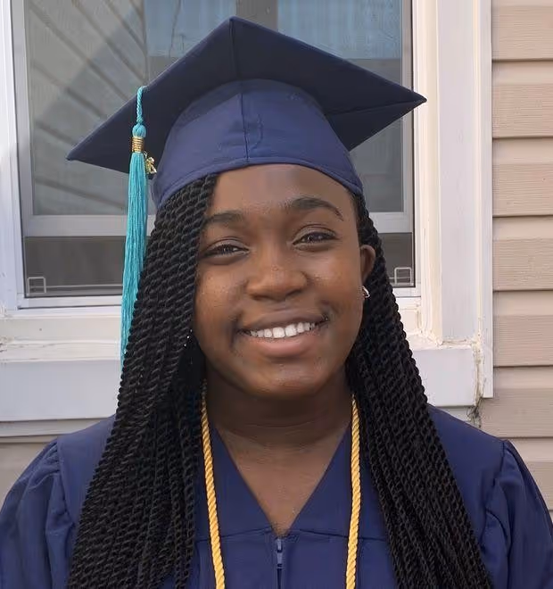Student in graduation cap and stole smiling outdoors.